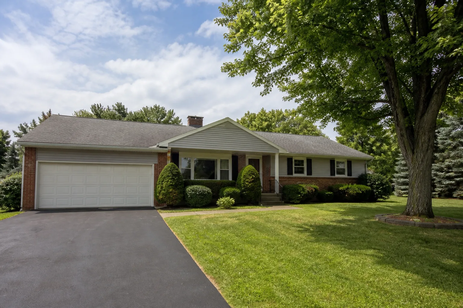 Well-kept brick and gray-siding ranch home with a broad lawn and mature tree