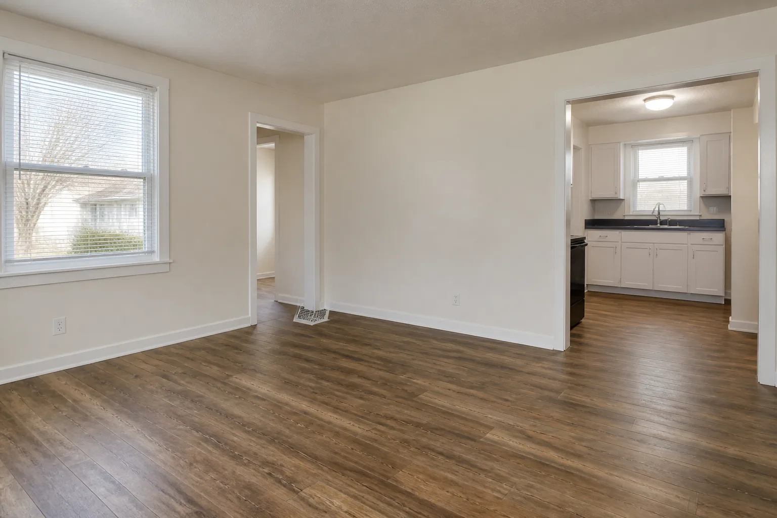 Empty refreshed rental living space with clean flooring, painted walls, and compact kitchen